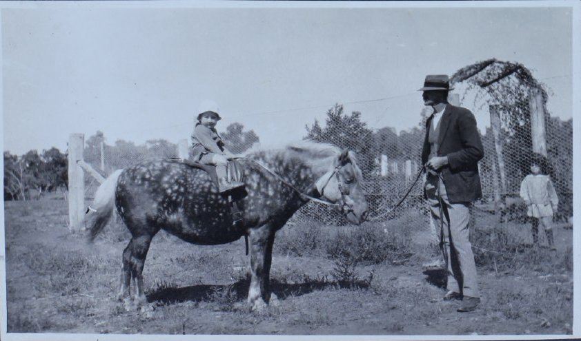 Man leading a pony with a young girl on its back, and another child standing