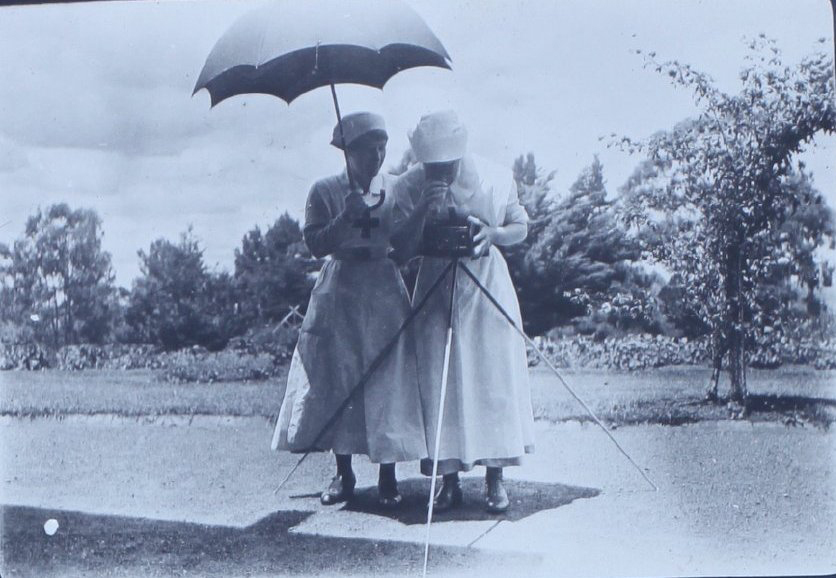 Two nurses under an umbrella with a camera