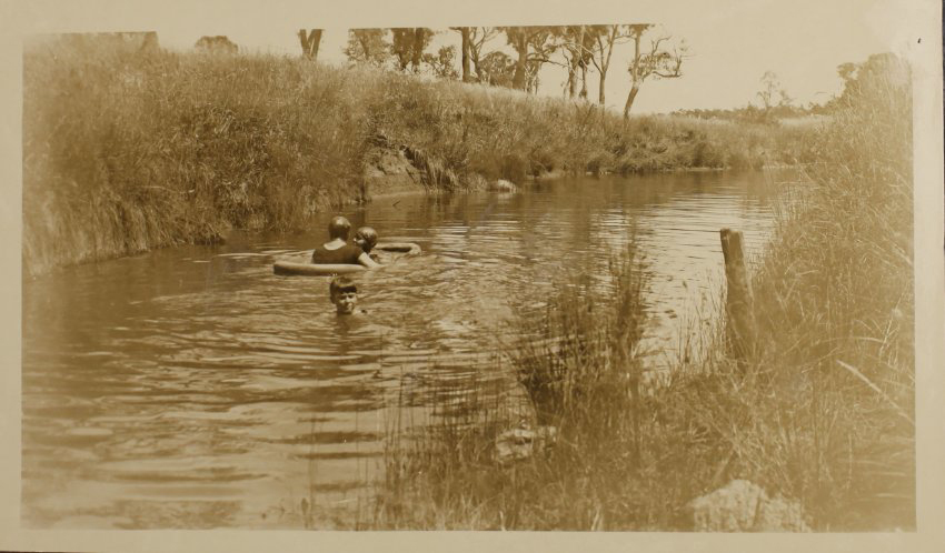 Unidentified woman and two children swimming in the creek