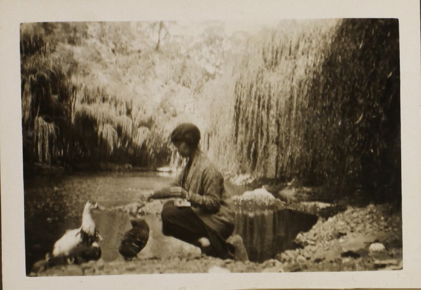 Unidentified woman with ducks beside the creek