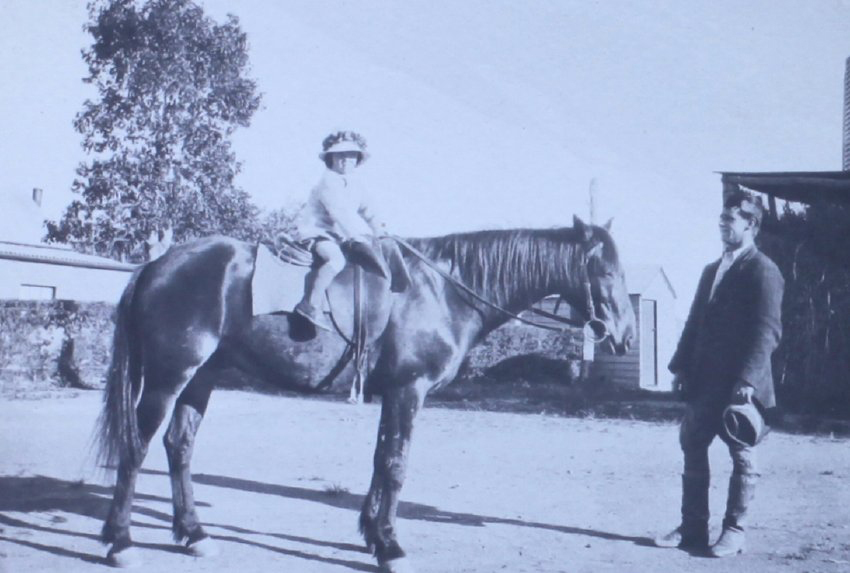 Young girl on a horse with a man watching on