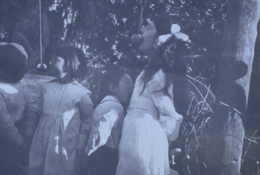 Four young children trying to eat apples on string
