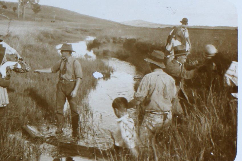 Group of men, women and children crossing a creek