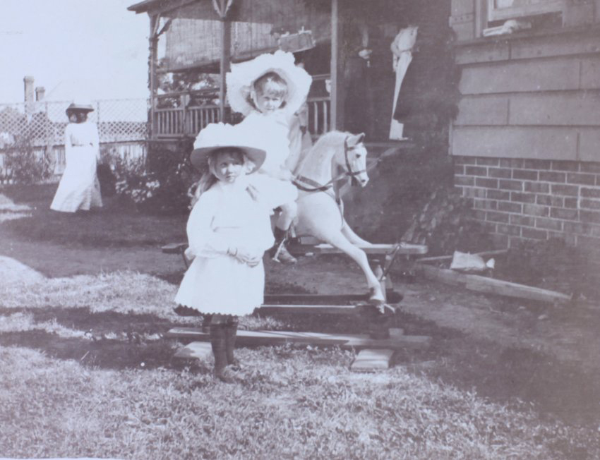 Young girl riding a rocking horse with another girl standing in front of the horse