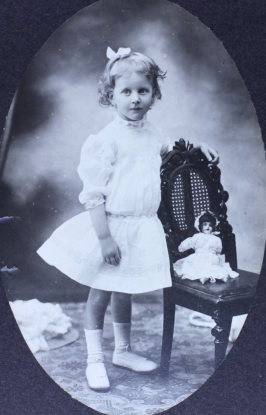 Young girl standing beside a chair with a doll sitting on the chair