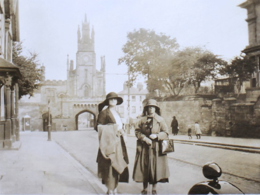 Two women standing on the street in front of a large gateway