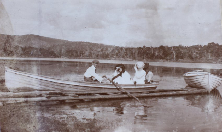 Man and three women sitting in a boat on the edge of a lake[?]