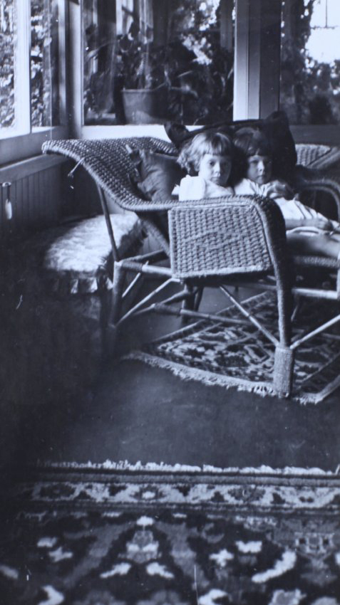 Two small girls sitting on a cane lounge in a sunroom