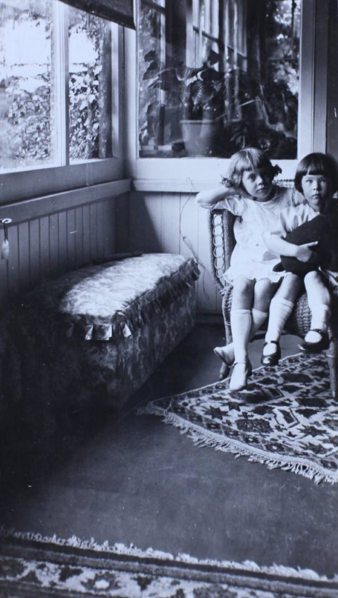 Two young girls sitting in a cane chair in a sunroom