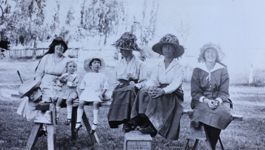 Group of women and children sitting on a plank in the garden