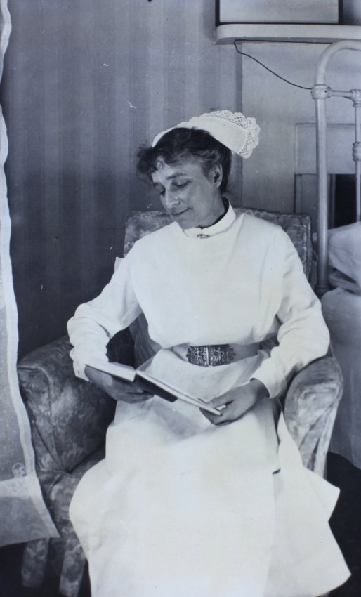 Nurse sitting in a chair beside a bed reading