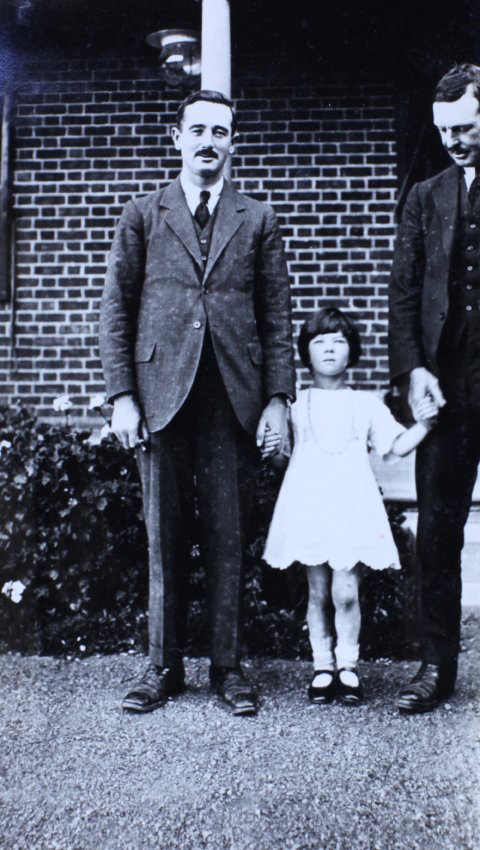 Two men and a girl standing in front of a house