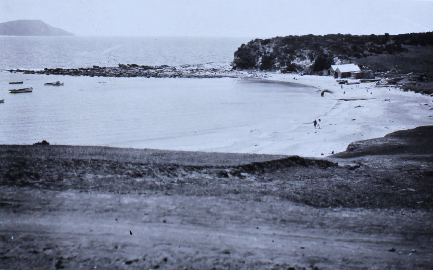 View of a small beach, boats in the water and the ocean beyond