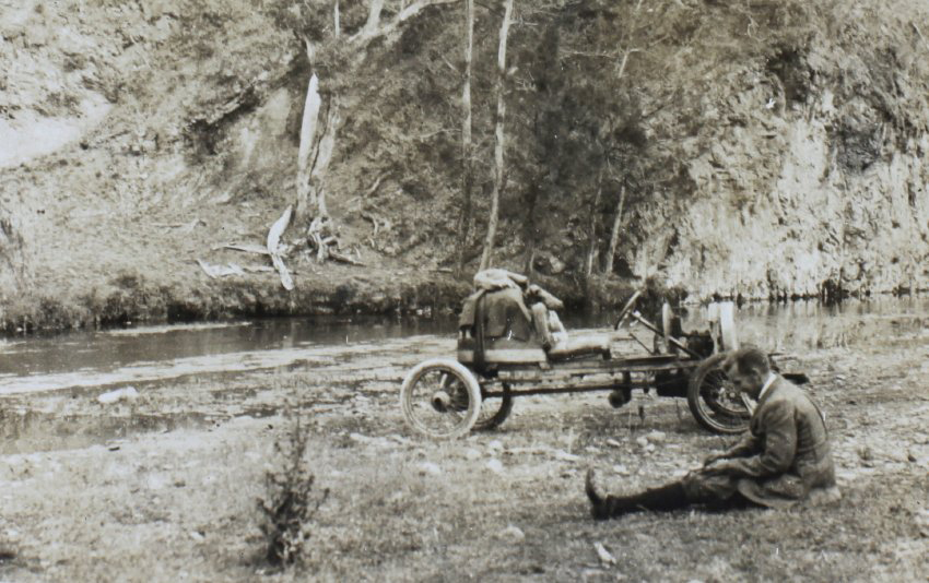 Unidentified man sitting on the grass beside a creek