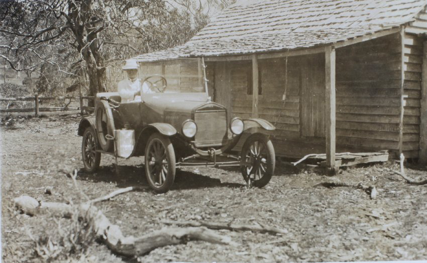 Driver and car sitting outside a bush hut