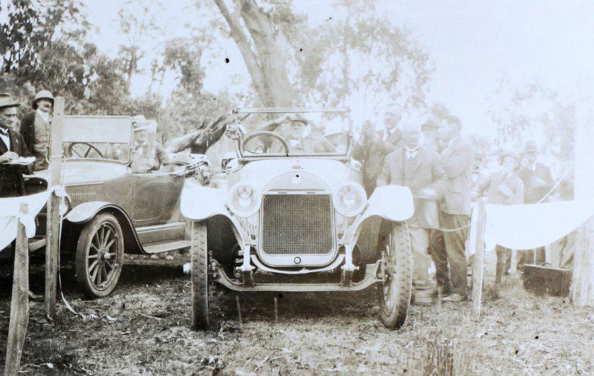 Group of unidentified men standing around a man seated in a car