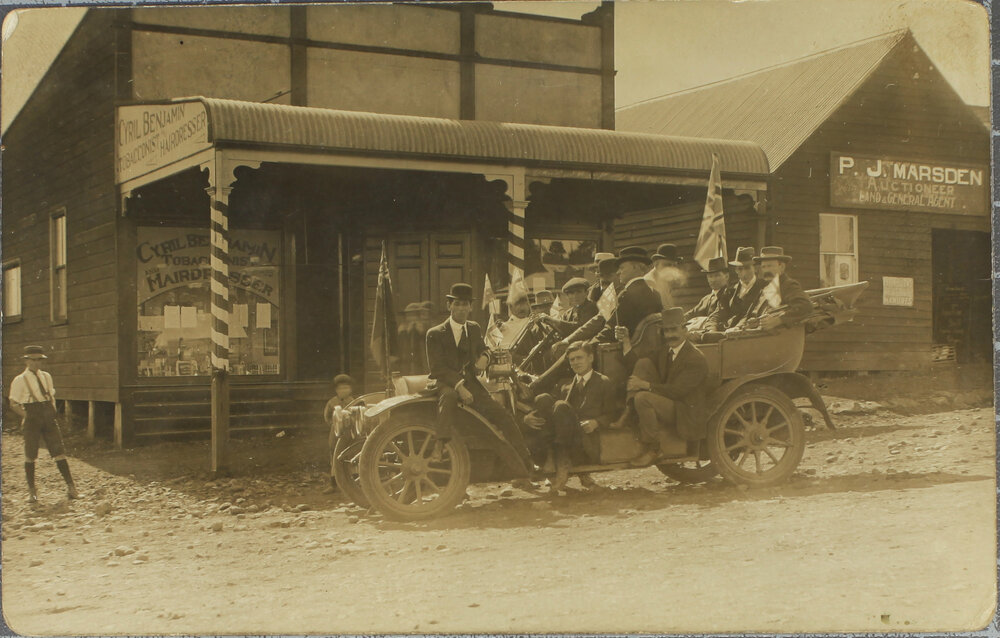 Men in car outside Cyril Benjamin, Tobacconist / Hairdresser