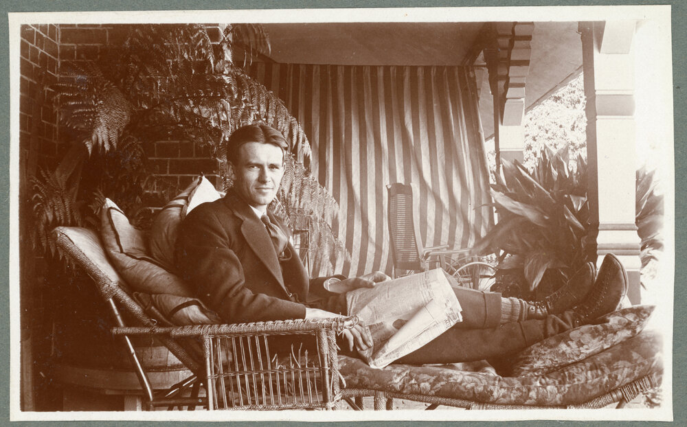 Man lounging with a newspaper at Booloominbah, c.1919
