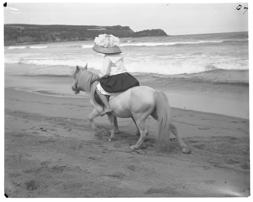 Girl riding a pony along a seashore, 1907