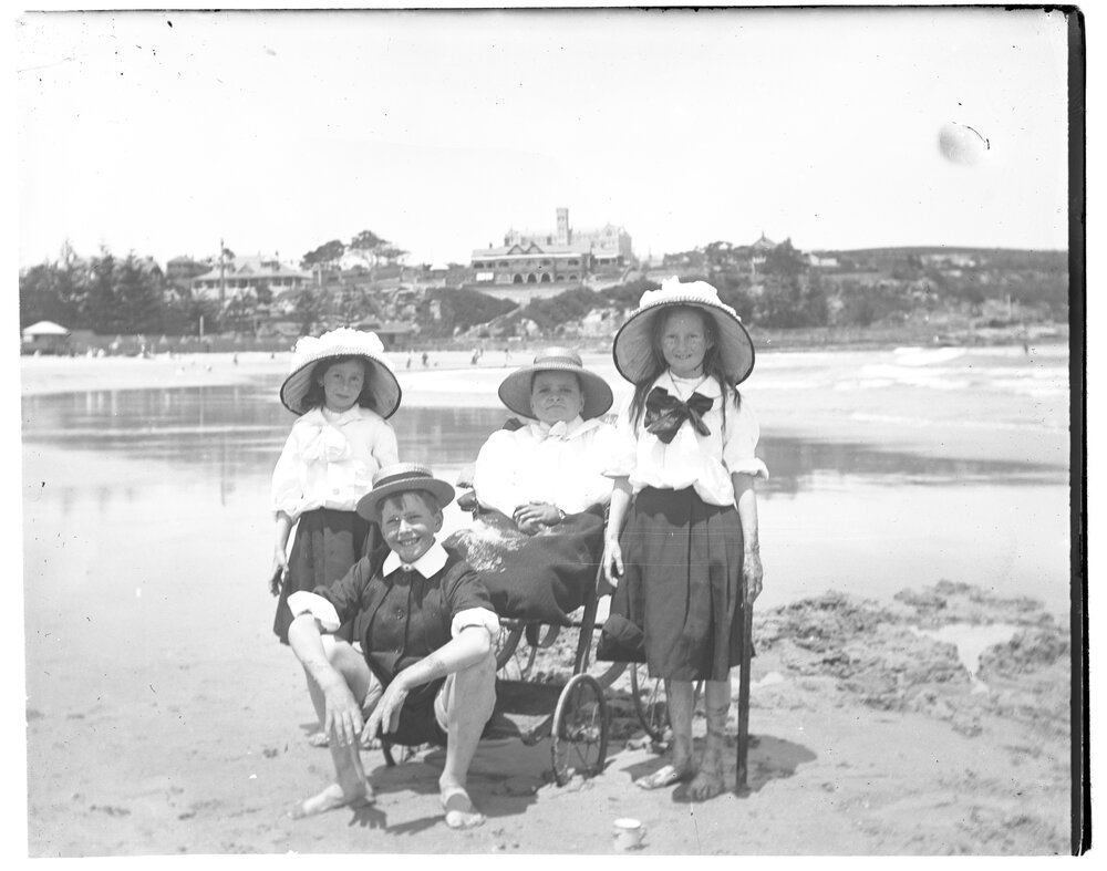A woman in a wheelchair with two girls and a boy on a beach, 1907