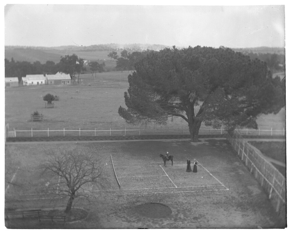 Elevated view of a tennis court with two women and a child on horseback