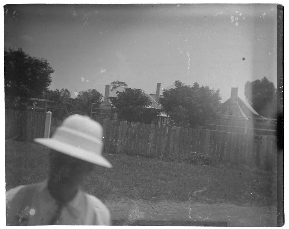 A man in a hat standing in front of a fenceline