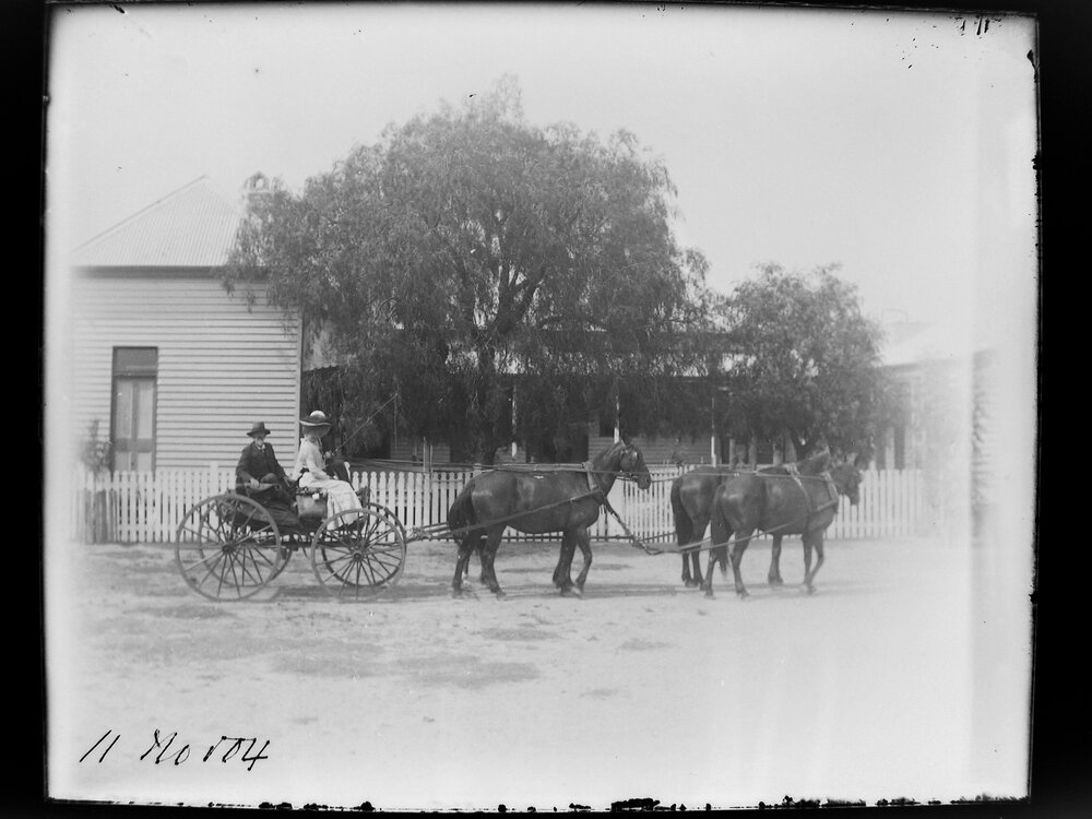 One man and women outside a house in a horse-drawn carraige