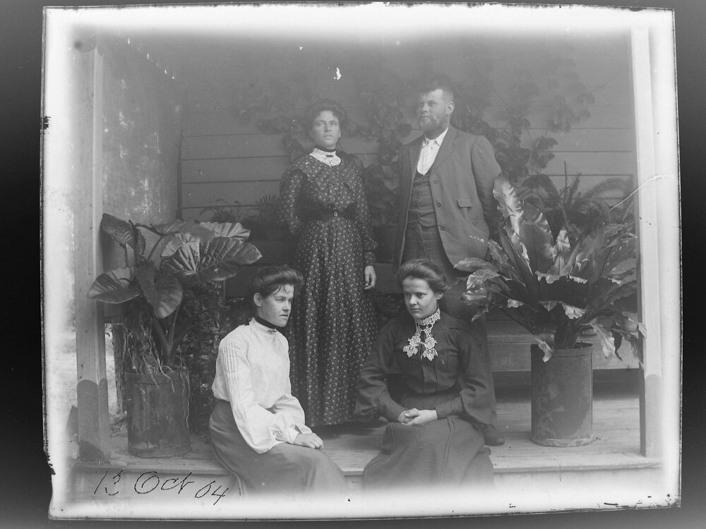 Three women and a man on a verandah with potted plants, 1904