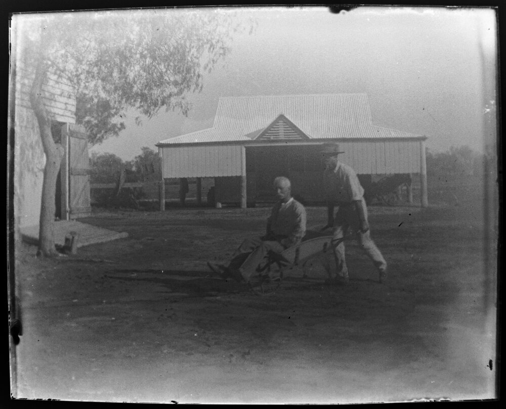 Man pushing another man in a wheelbarrow