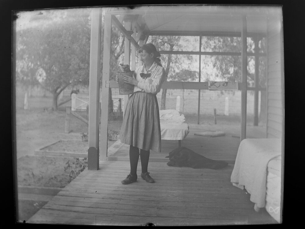 Woman on verandah holding a possum in a bucket