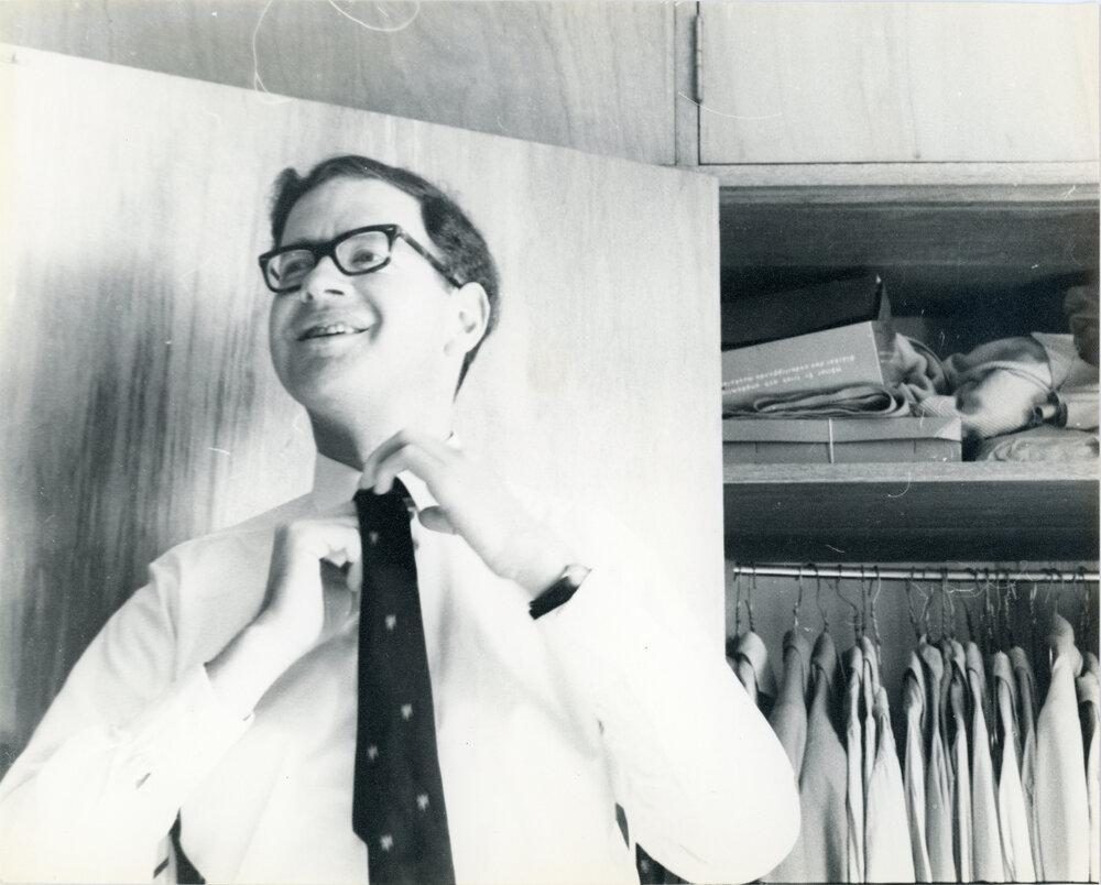John Ryan adjusting his tie in front of a closet