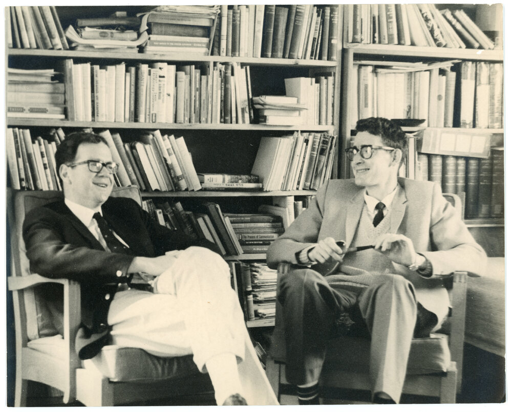 John Ryan and another gentleman seated in front of bookshelves