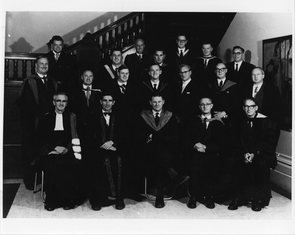 Group of men in academic dress beneath a staircase