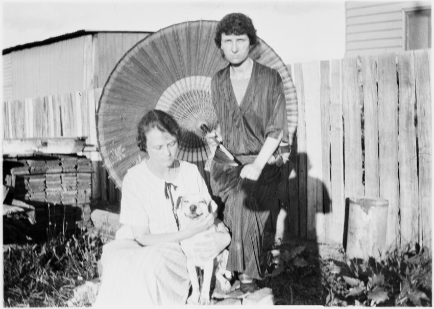 Clare Chamberlain (seated with dog) and Vere Chamberlain in front of a parasol and paling fence