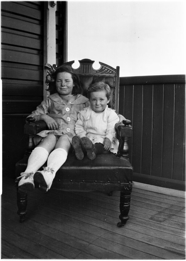 Two unidentified children sitting on a chair on the verandah of 63 Barney Street, Armidale