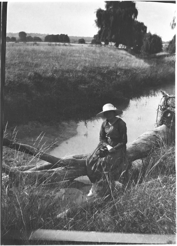 Unidentified woman sitting on a log by a creek