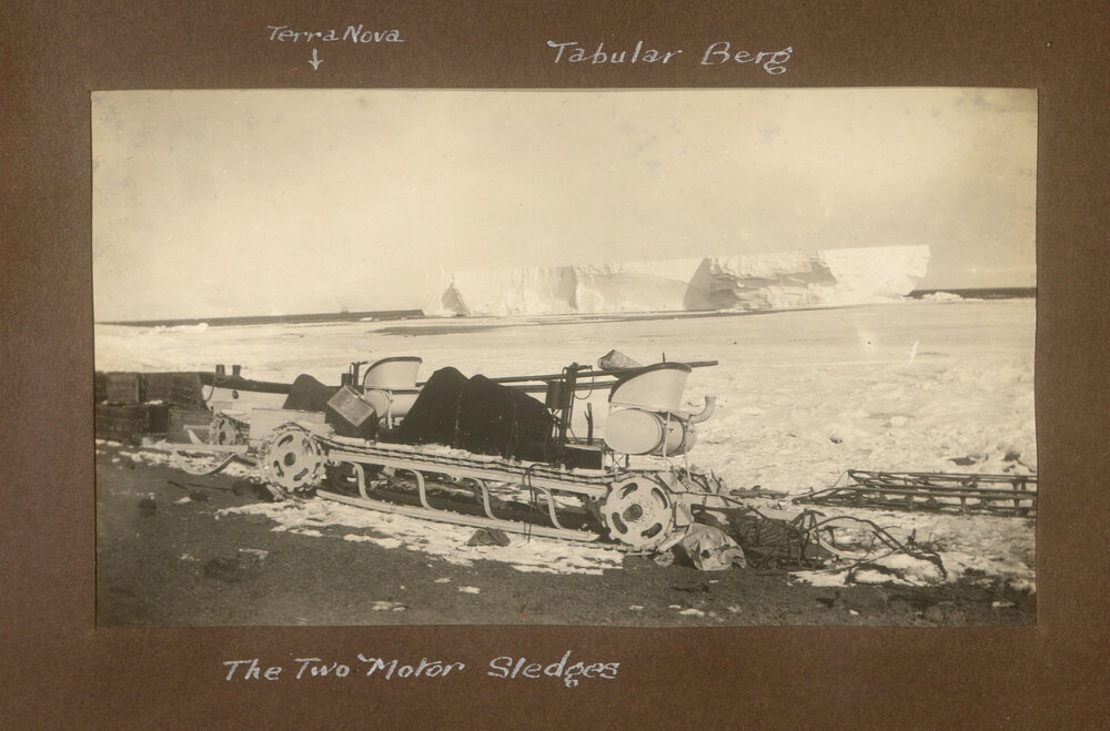 Two motor sledges at Cape Evans, showing a large tabular iceberg &amp; the Terra Nova in the background