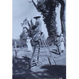 Woman sitting atop a ladder, with another woman and two nurses in the background