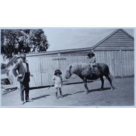 Man leading a pony with a young girl on its back, and another child standing