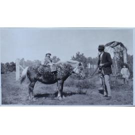 Man leading a pony with a young girl on its back, and another child standing