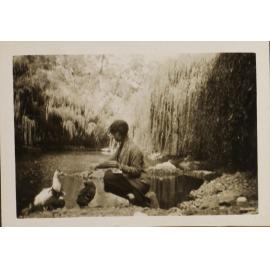 Unidentified woman with ducks beside the creek