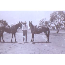 Unidentified man holding two horses