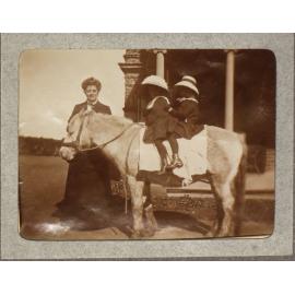 Two unidentified girls on a pony with an woman