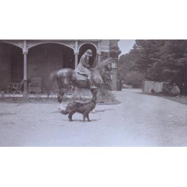 Unidentified woman on a horse on the driveway with a pet dog