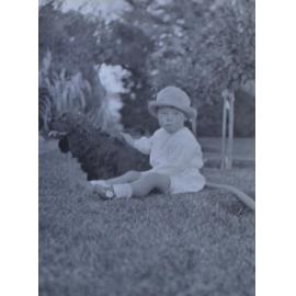 Unidentified child sitting on the lawn with a pet dog
