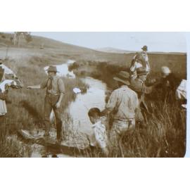 Group of men, women and children crossing a creek