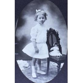 Young girl standing beside a chair with a doll sitting on the chair