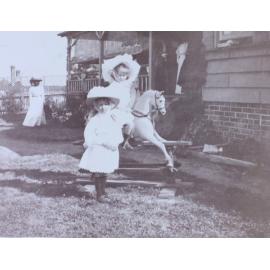 Young girl riding a rocking horse with another girl standing in front of the horse