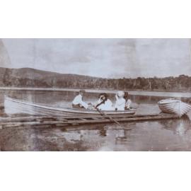 Man and three women sitting in a boat on the edge of a lake[?]