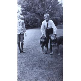 Two young boys on the lawn with one holding two pet dogs